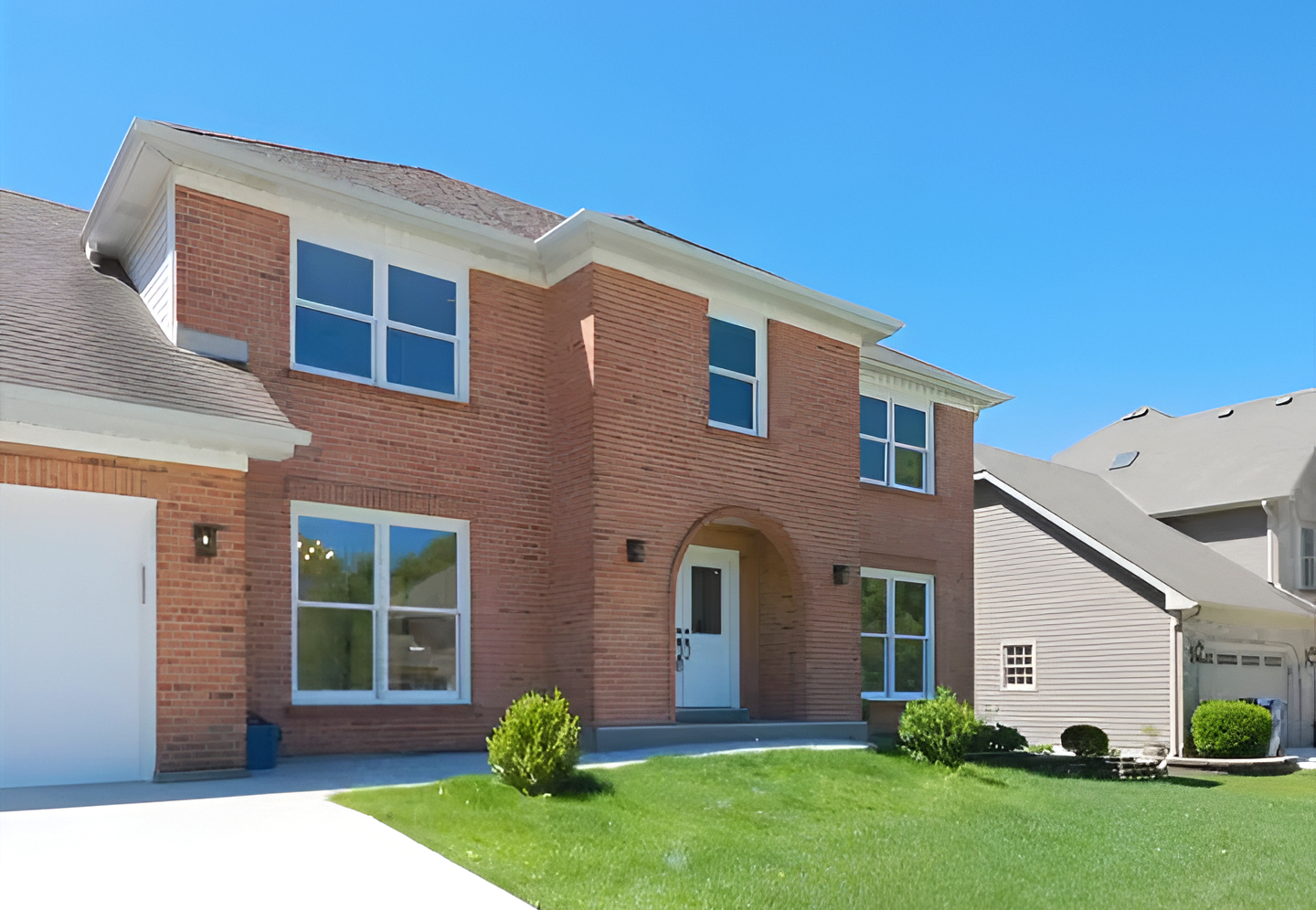 Two-story brick house with large windows, a white front door, and a manicured lawn under a clear blue sky.